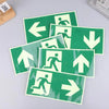 A collection of photoluminescent emergency exit sign decals showing various directional arrows on a green background.