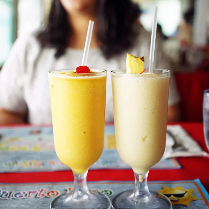 A close-up of a yellow margarita drink in a glass with a straw, set on a red table.