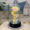 A glass dome containing an eternal rose with a glowing yellow LED light, displayed on a black base.
