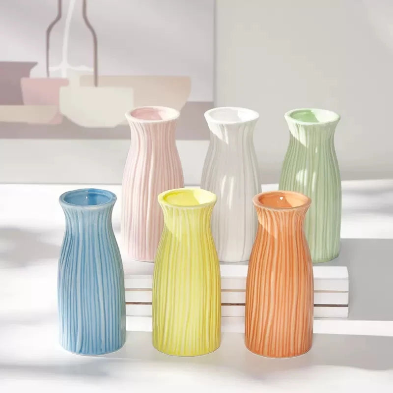 A collection of ceramic bud vases in pastel shades of pink, green, and yellow arranged on a white surface.