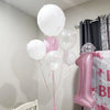 A cluster of pink and white latex balloons is displayed next to a pink birthday cake.