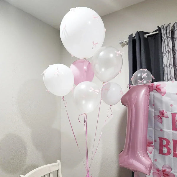 Un grupo de globos de látex rosa y blanco junto a un pastel de cumpleaños rosa.
