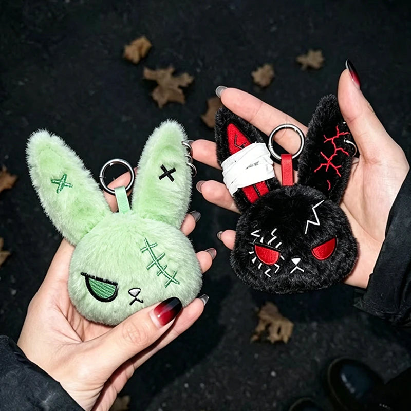 A hand holds a dark black bunny plush keychain with red accents and green eyes against a dark background.