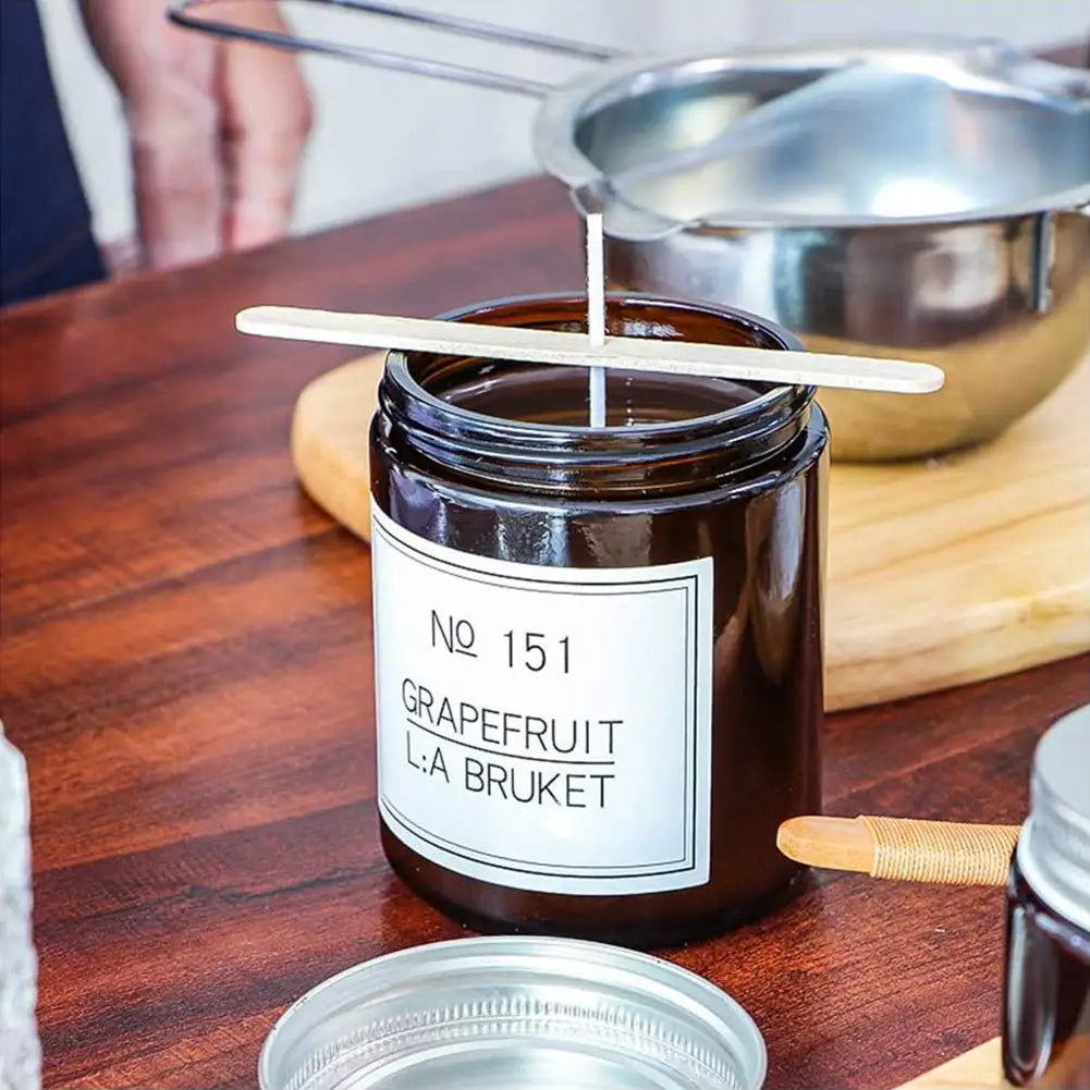 A glass jar of dark brown liquid labeled No 151 Grapefruit L:A Bruket with a wooden stick used to stir.