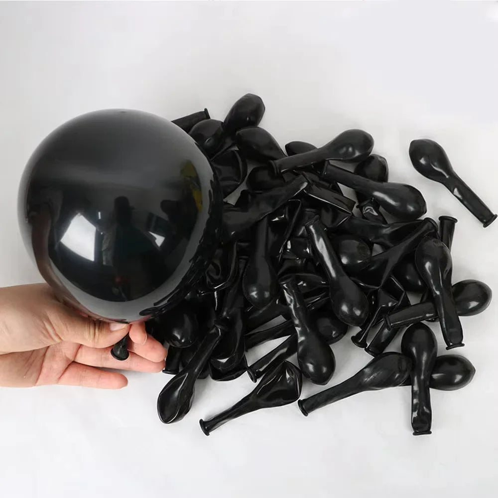 A hand holds a black football balloon party set with number foils, showing many small black balloons.