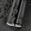 Roll of vintage black floral self-adhesive contact paper lying on a dark surface.