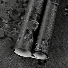 Rouleau de papier contact floral noir vintage autocollant posé sur une surface sombre.