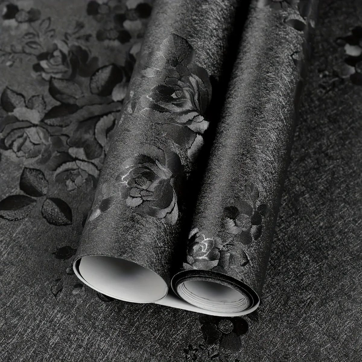 Roll of vintage black floral self-adhesive contact paper lying on a dark surface.