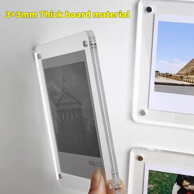 A transparent acrylic photo frame with a magnetic display stand mounted on a white wall.
