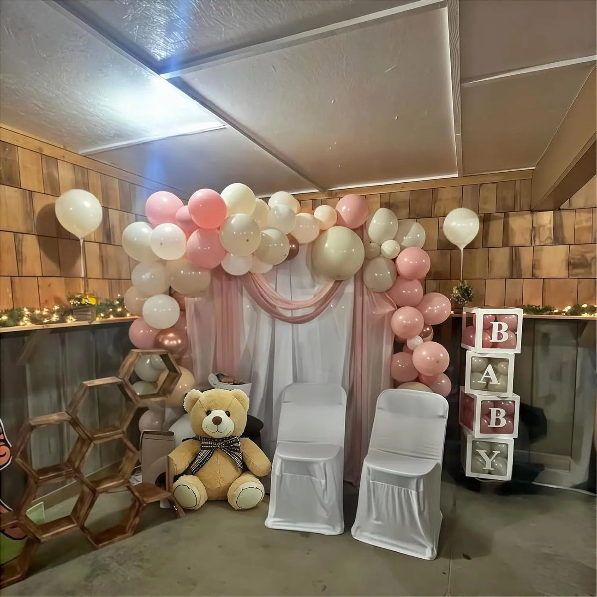 A display of pink, sand, and gold balloons decorated with sheer fabric and a teddy bear for an event backdrop.