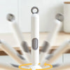 A white adjustable long-handled brush with six bristles is shown on a wooden surface.