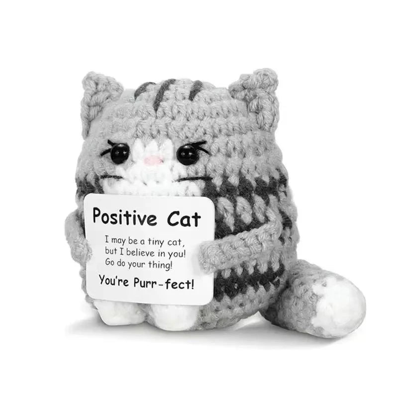 A handmade knitted plush cat toy with gray and white fur and a sign that reads You're Purr-fect