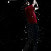 A man in a red shirt is shown swinging a golf club against a black background, creating a spray of white particles.