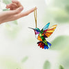 A colorful acrylic hummingbird suncatcher ornament hanging by a gold string against a soft green background.