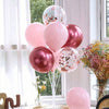 A bouquet of pink and rose gold balloons on a white stand, decorated with gold confetti, in a bright room.