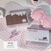 Lazo de tela a cuadros rosas junto a una caja rectangular de chocolate y una taza de té blanca sobre una superficie de lunare