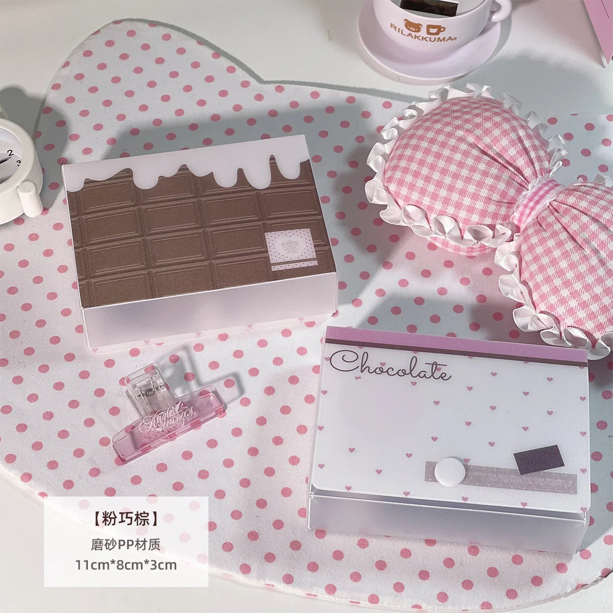 Lazo de tela a cuadros rosas junto a una caja rectangular de chocolate y una taza de té blanca sobre una superficie de lunare
