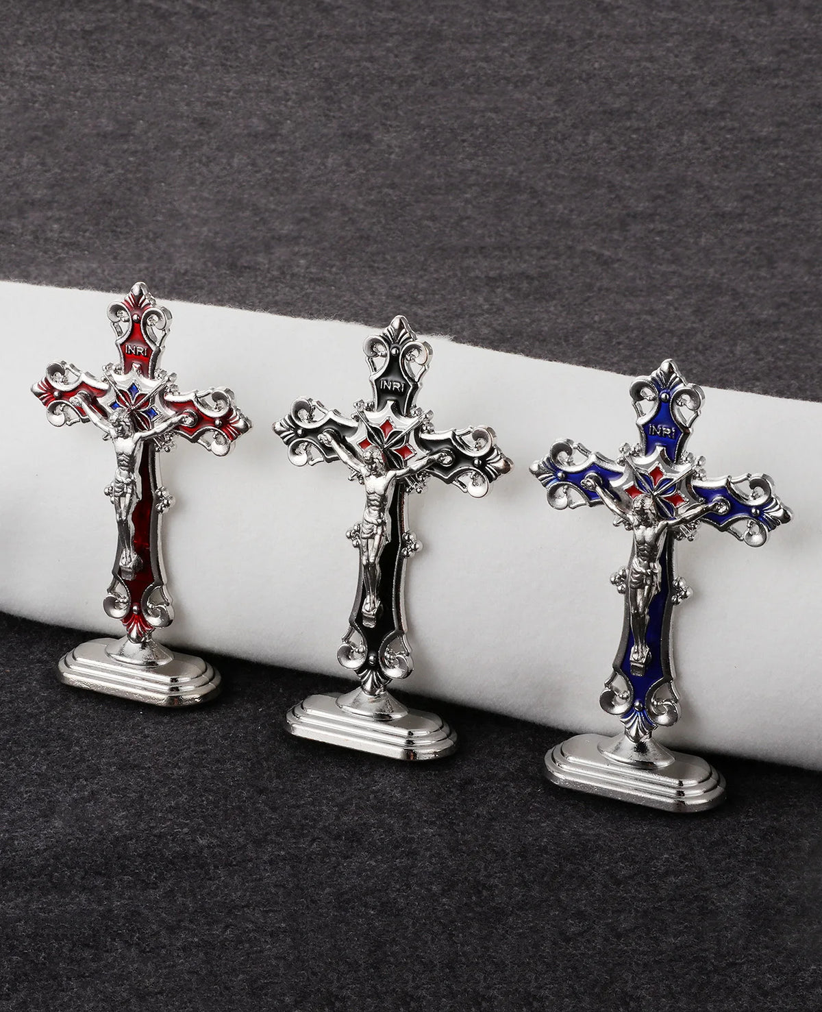 Three ornate metal crucifix desk crosses with self-adhesive bases displayed on a dark surface.