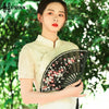 A woman in traditional attire holds an elegant black folding fan decorated with red and white plum blossoms.