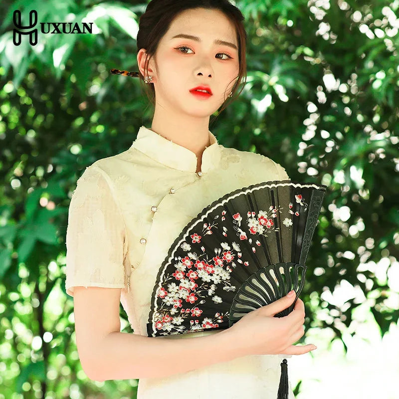 A woman in traditional attire holds an elegant black folding fan decorated with red and white plum blossoms.