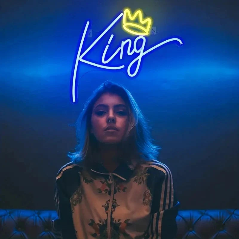 A woman looking at the camera under a neon sign that spells out King with a crown above it.