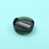 A dark green replacement tumbler lid with a silver-colored sliding mechanism resting on a light blue surface.