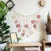 Bohemian macrame leaf wall hanging with pink and cream tassels displayed on a white wall.