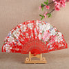 A vibrant red silk flower folding fan with pink and white floral patterns displayed on a wooden stand.