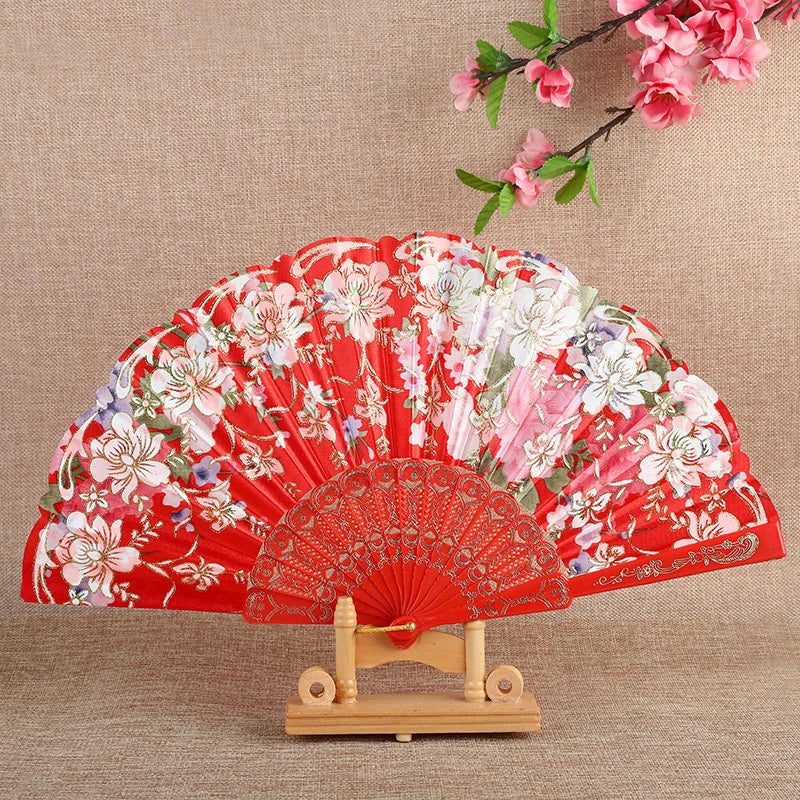 A vibrant red silk flower folding fan with pink and white floral patterns displayed on a wooden stand.