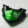 A green half face mask with a stylized eye design is shown in black protective gear.