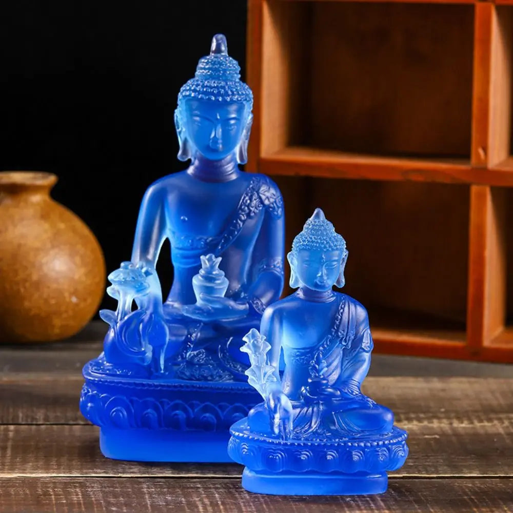 A blue resin statue of the Medicine Buddha seated in meditation on a wooden surface.