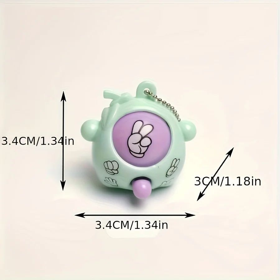 A small, light green keychain shaped like a face with a purple rock-paper-scissors symbol on it.