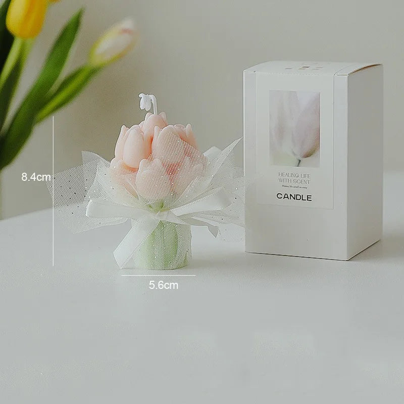 A white box candle with a pink tulip design sits next to a small arrangement of pink dried flowers.