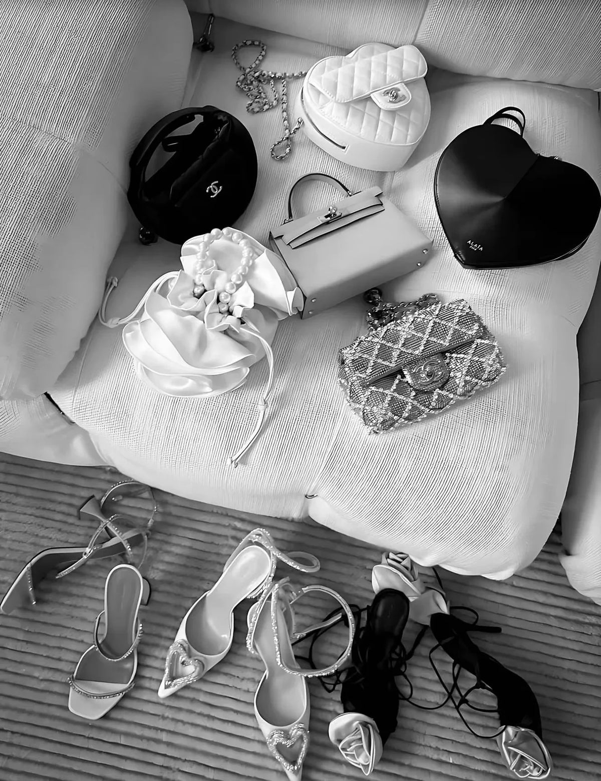 A collection of black and white accessories including handbags, jewelry, and high heels displayed on a light sofa.