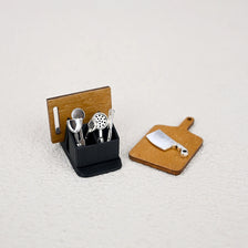 A miniature dollhouse kitchenware set with storage rack featuring silver utensils and a small knife on wooden blocks.