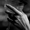 A hand holds a glass, featuring a ring, in a black and white photograph.