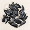 A collection of black obsidian arrow pendants scattered on a light beige fabric.