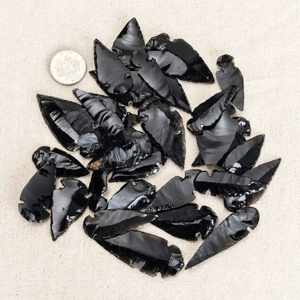 A collection of black obsidian arrow pendants scattered on a light beige fabric.