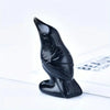 A black handcrafted obsidian crow statue with detailed feathers, resting on a white surface.