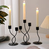 A set of black iron candle holders with white candles displayed on a white surface.