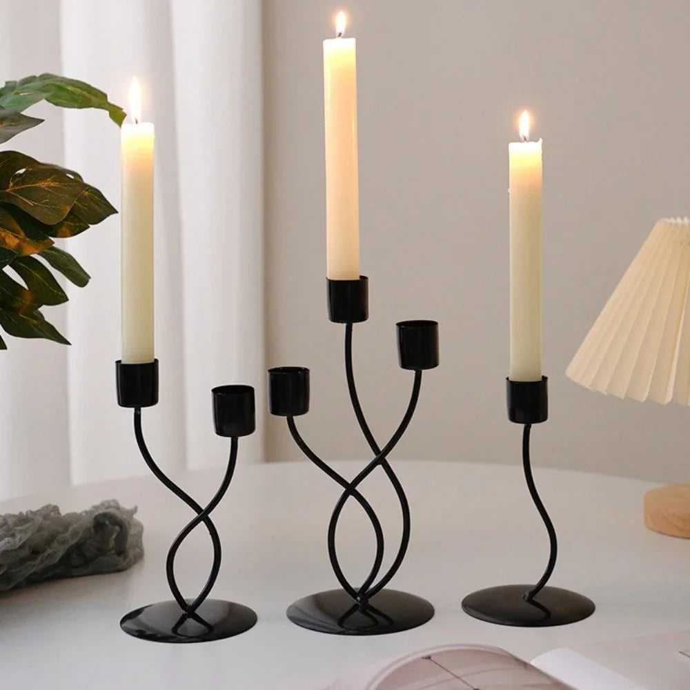 A set of black iron candle holders with white candles displayed on a white surface.