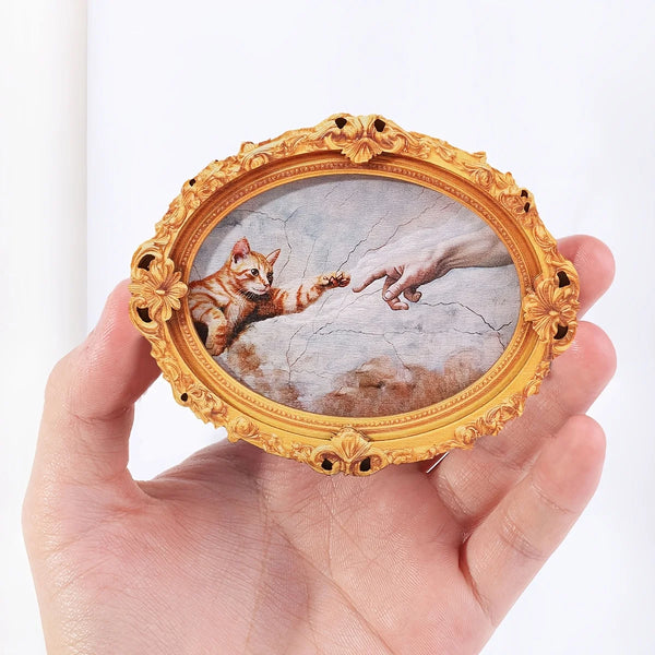 A hand holds a vintage oval frame with an ancient Greek style depiction of a cat and a human hand.
