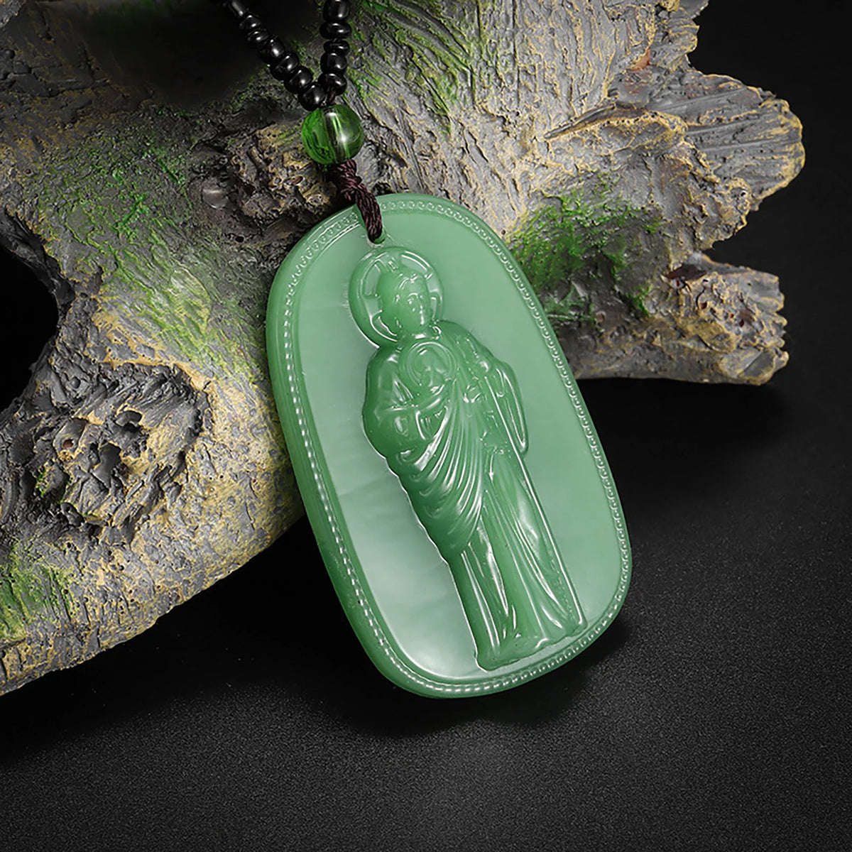 A green oval pendant depicting a figure, suspended from a dark beaded necklace and resting on a piece of textured wood.