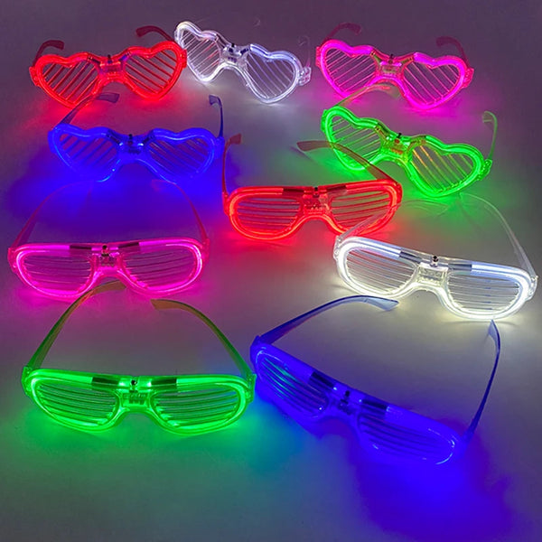 A collection of fluorescent heart-shaped LED party glasses glowing in various colors on a dark surface.