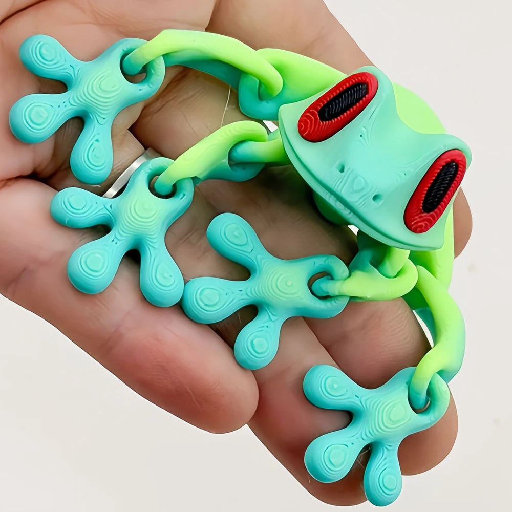 A hand holds a realistic 3D frog fridge magnet with movable joints in bright green and teal colors.