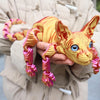 A hand holds a realistic Sphynx cat fidget toy with orange and pink striped fur against a beige jacket.