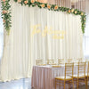 A wedding backdrop featuring sheer white curtains draped with greenery and floral accents, set up for an event.