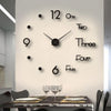 A modern wall clock with black numbers and hands is mounted on a white wall above a dining table.