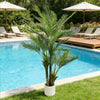 An artificial triple trunk palm tree standing in a white pot next to a blue swimming pool.