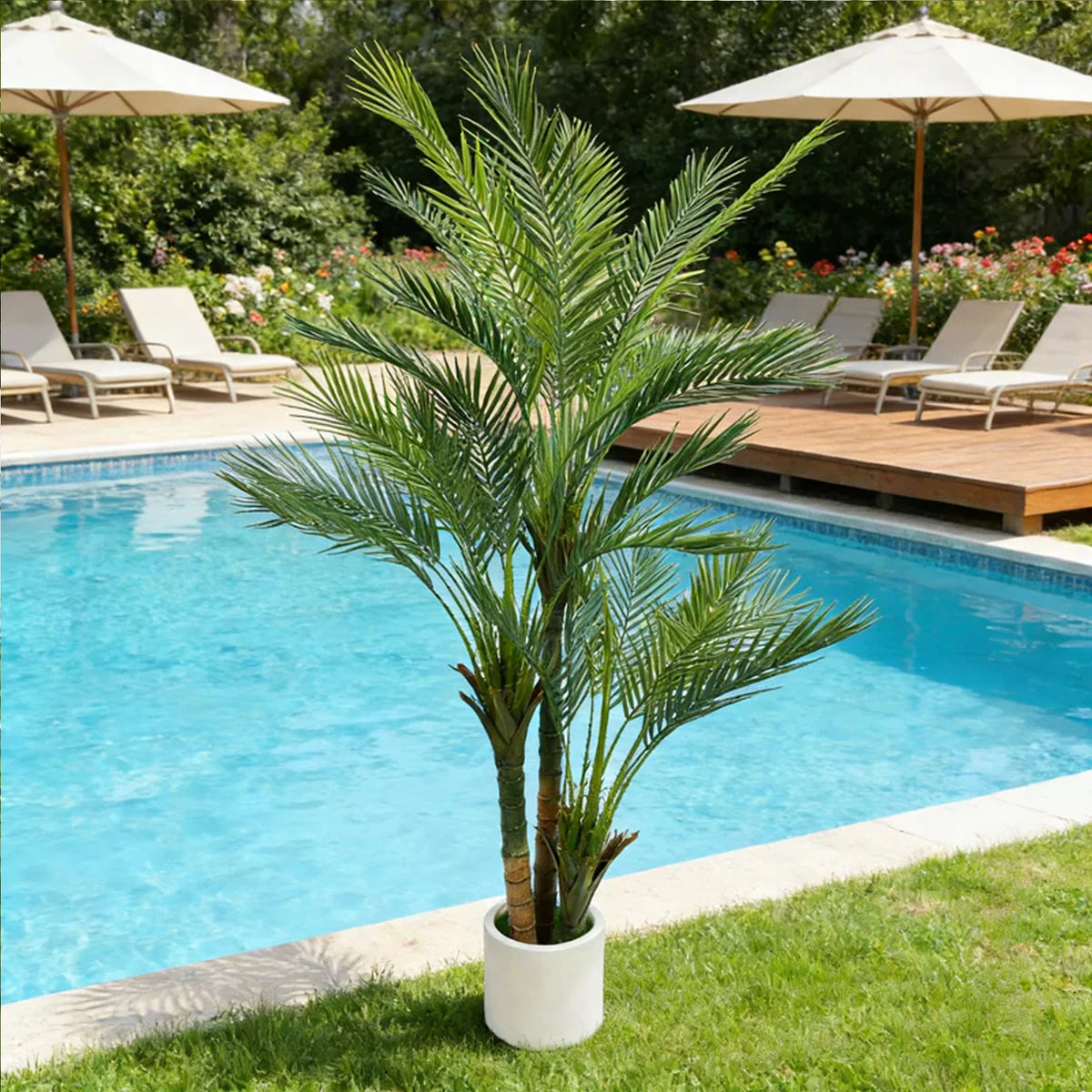 An artificial triple trunk palm tree standing in a white pot next to a blue swimming pool.